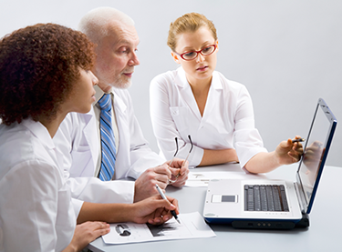 Photo of three people looking at a laptop computer